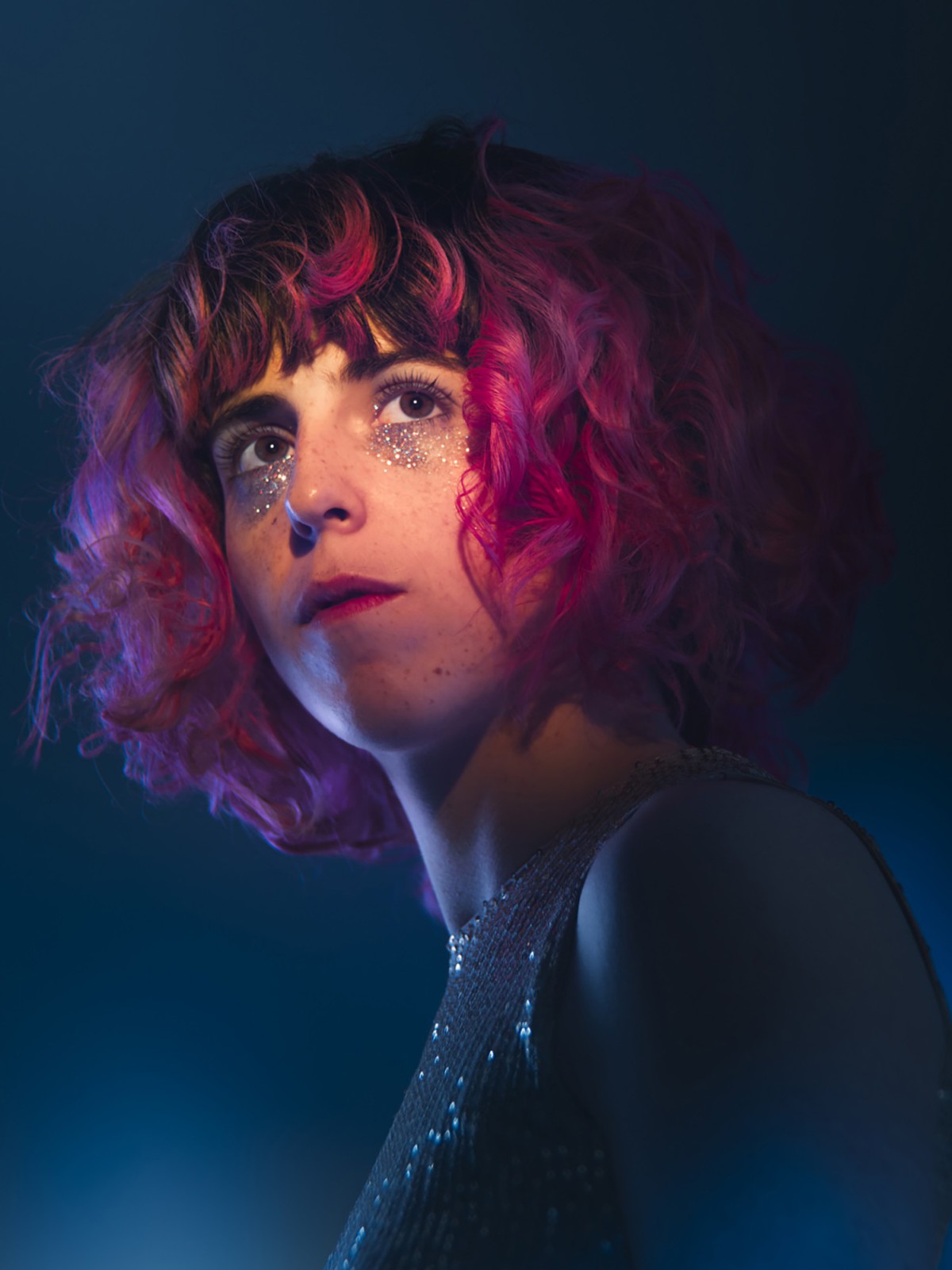 A portrait of the musician Knobil with red curls and glittering makeup