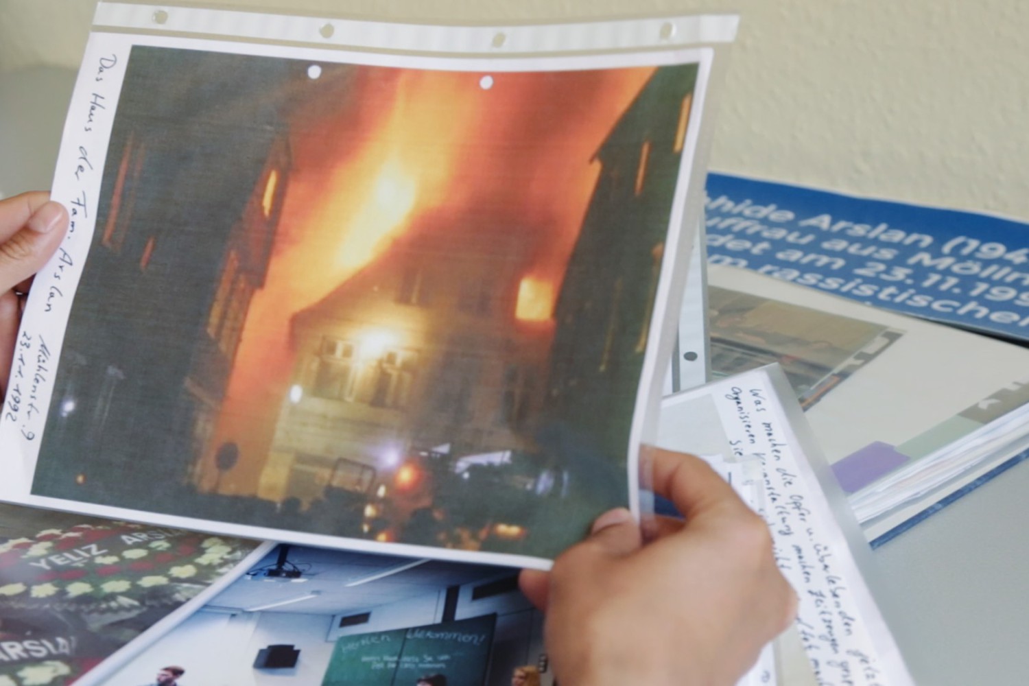 Szene aus dem Film "Der zweite Anschlag". Eine Person hält ein Foto, auf dem man ein brennendes Haus sieht.