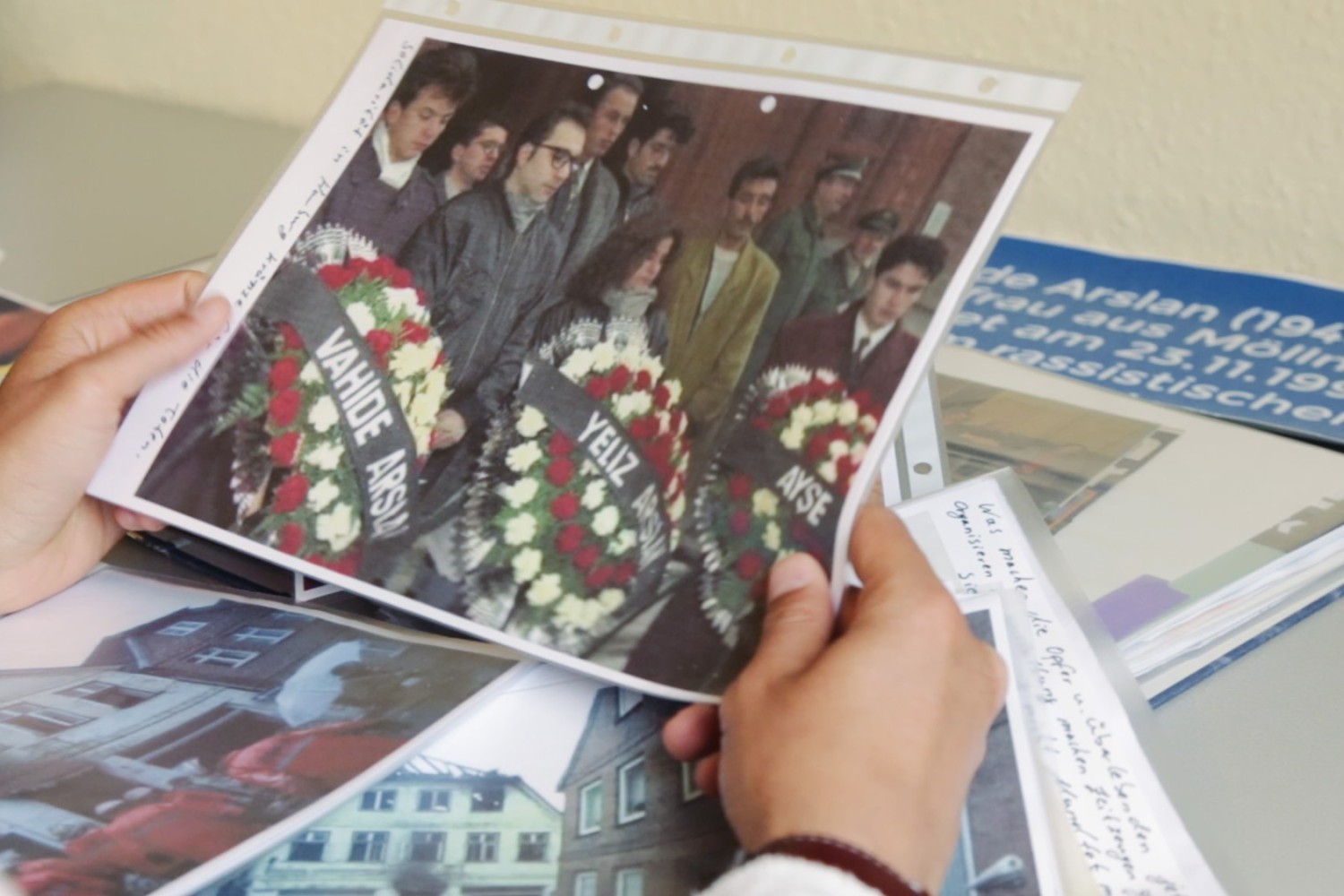 Szene aus dem Film "Der zweite Anschlag". Eine Person hält ein Foto, auf dem Menschen mit Trauerkränzen zu sehen sind.