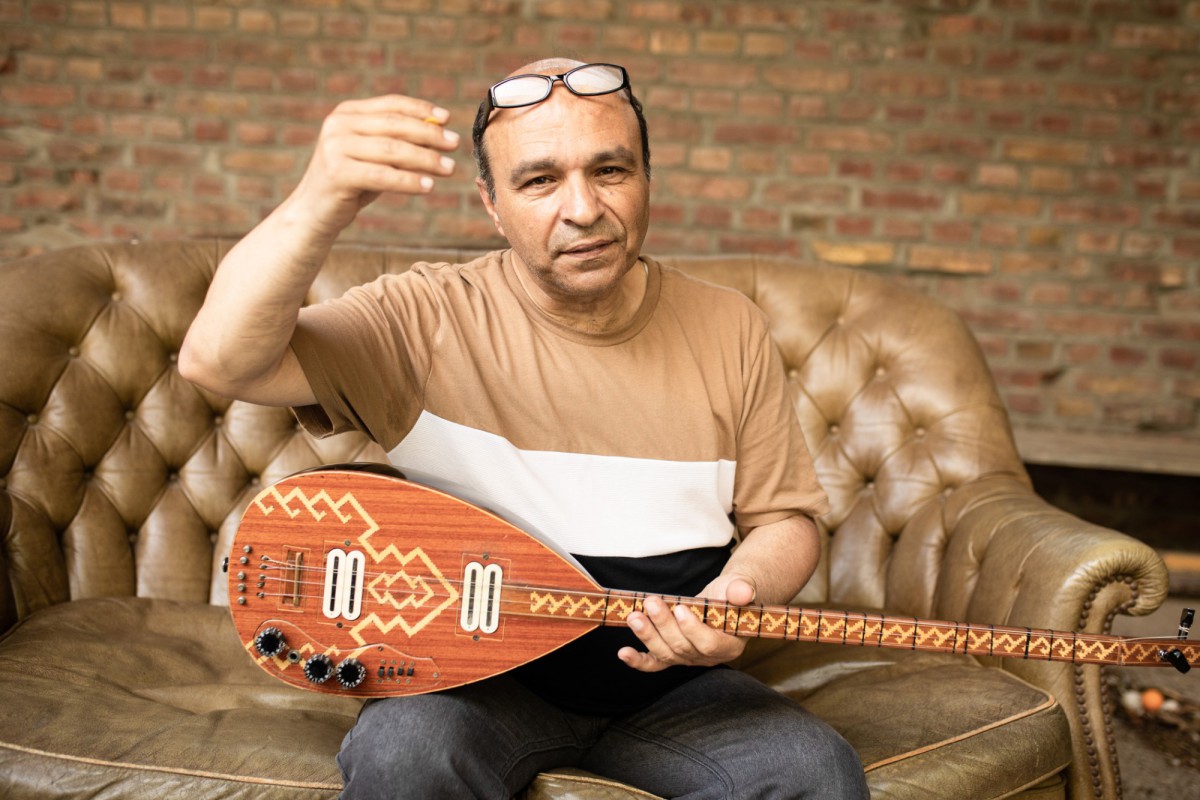 Ata Canani sitzt mit seiner Bağlama auf einem braunen Ledersofa