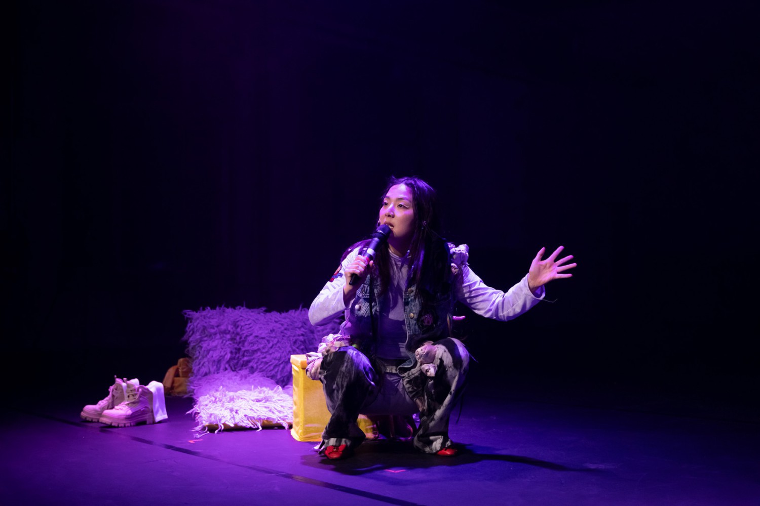 Hyunsin Kim squats on stage and sings into a microphone.