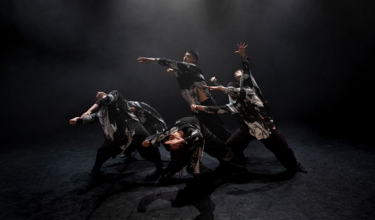 Eine Gruppe von Tänzer*innen in schwarz weißer Kleidung in Nebel gehüllt