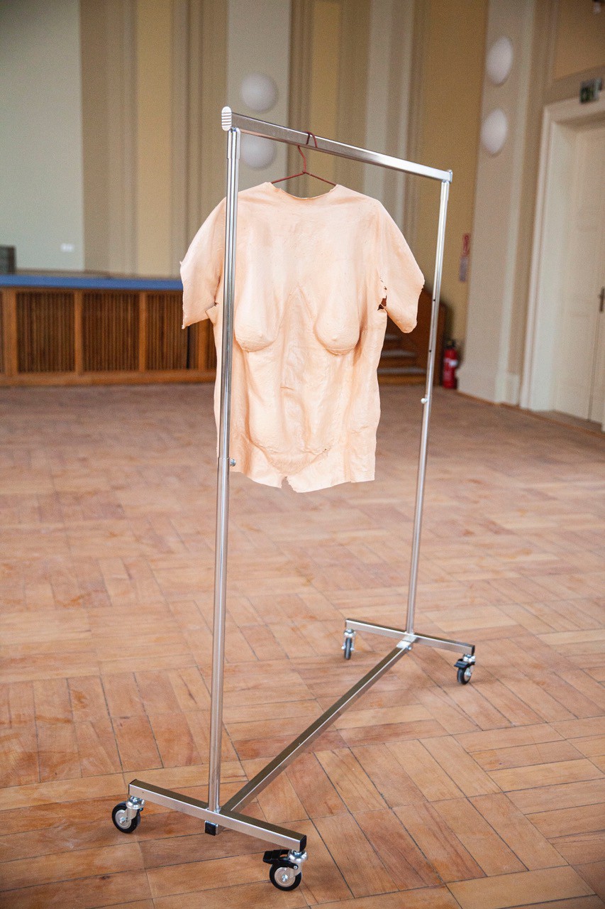 Ein Kleiderständer in einem leeren Saal, an dem ein Fatsuit hängt