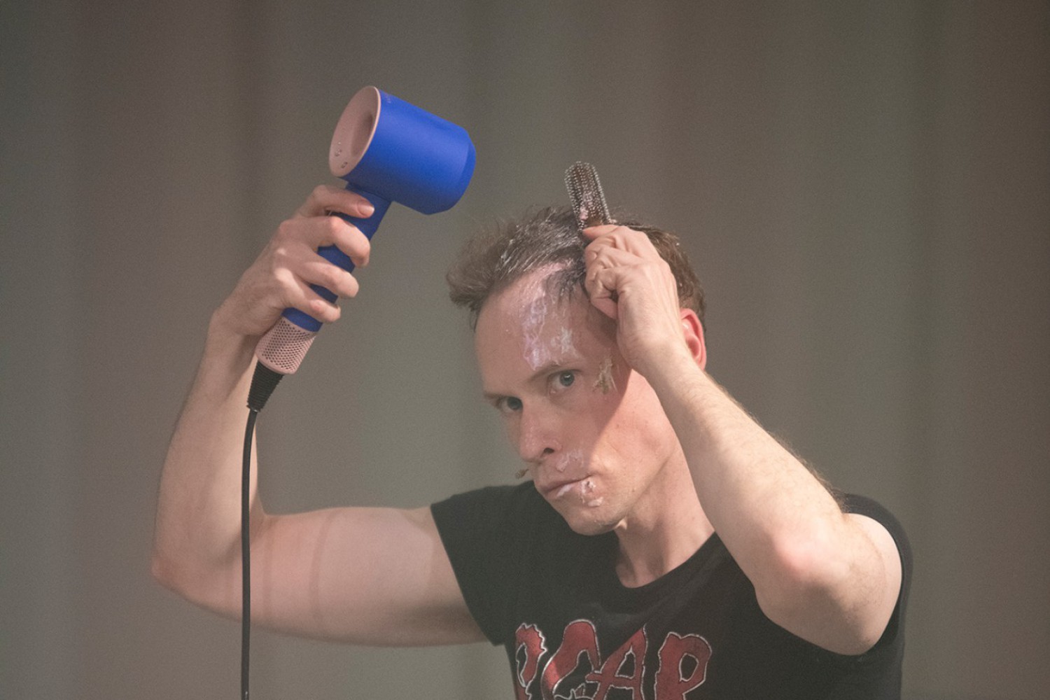 Hendrik Quast sitzt im Jogginganzug auf einem Bett und föhnt sein Haar