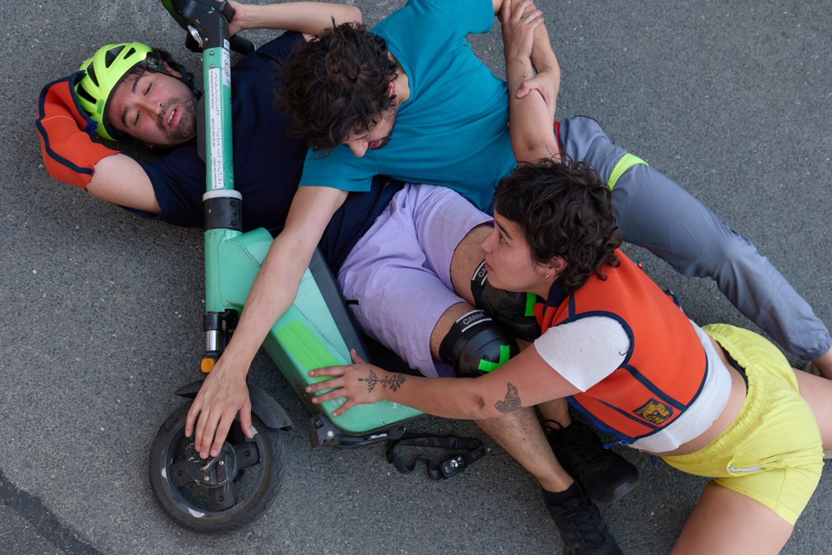 Tremenda Corporea liegen mit einem E-Scooter auf dem Asphalt als seien sie gestürzt