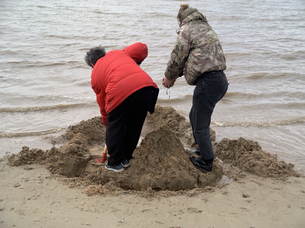 Zwei Personen graben im Sand an einem Strand