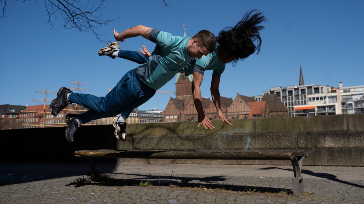 Zwei Performer schweben springend in Seitlage in der Luft. Im Hintergrund der Bremer Dom und die Schlachte.