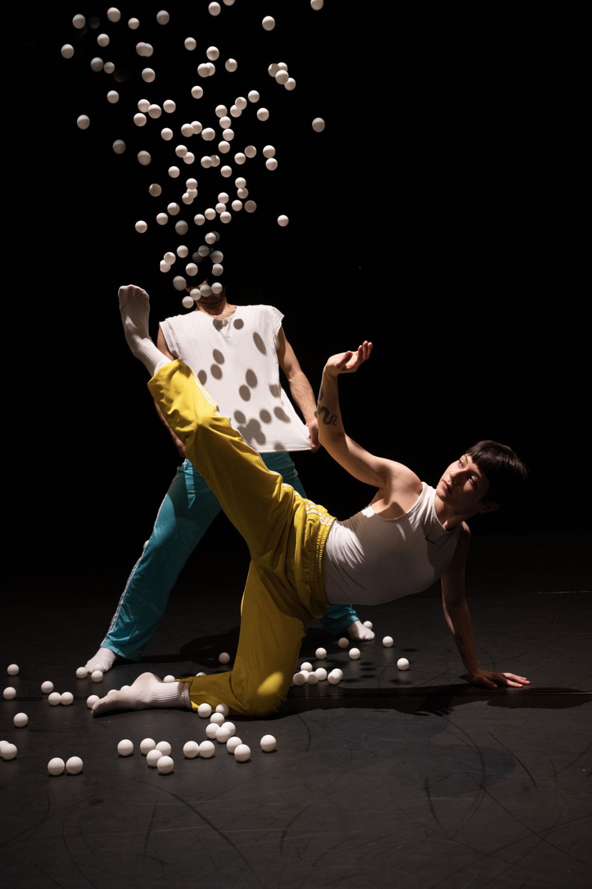 Two dancers in movement with many falling Ping Pong balls