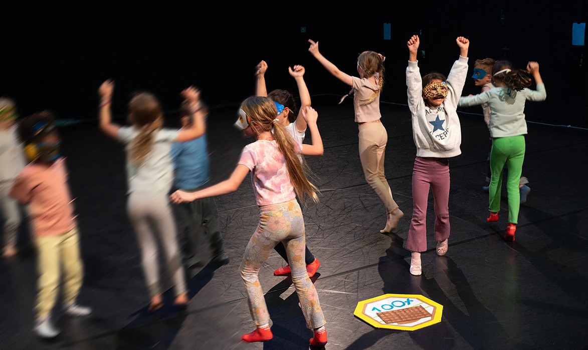 eine Gruppe von Kindern hüpfen auf der Bühne und recken die Arme nach oben